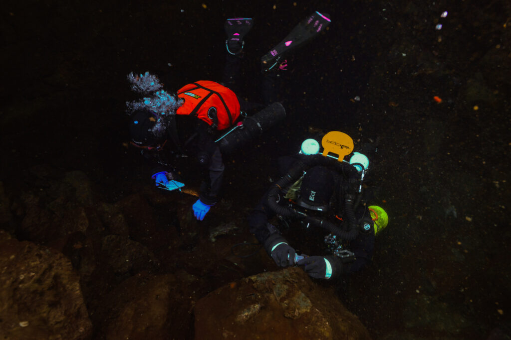 Two divers with lights over a dark lava seabed