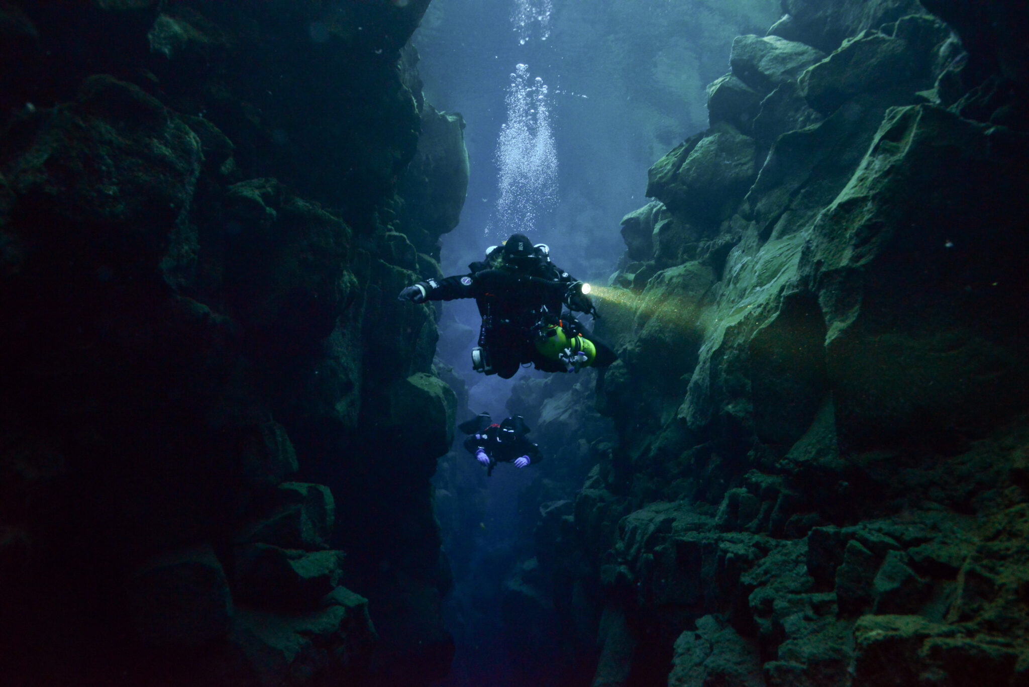 Two divers with a torch in a narrow underwater fissure in Iceland