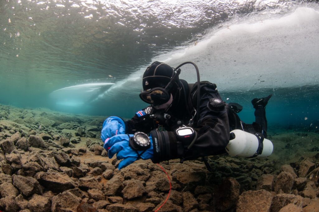 Diver with a redundant cold-water setup on the lakebed beneath a ceiling of ice