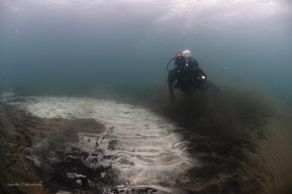 潜水员在 Kleifarvatn 湖底的白色地热沉积物旁