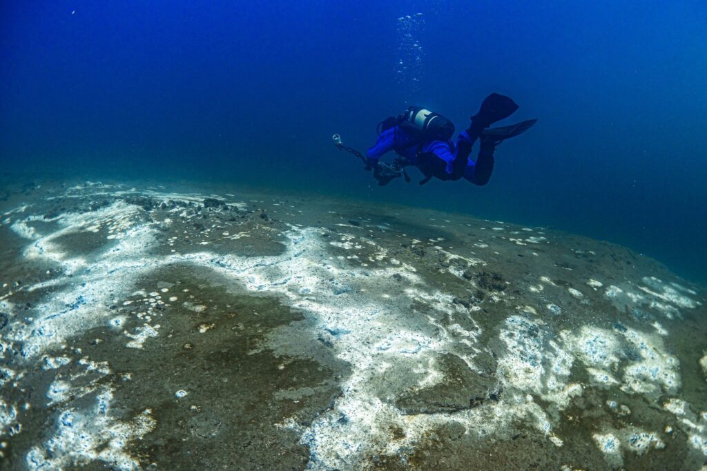 Diver in a blue dry suit over the white geothermal deposits on the bed of Kleifarvatn